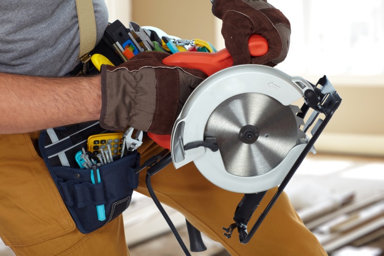Construction Worker hands with circular saw over house background.