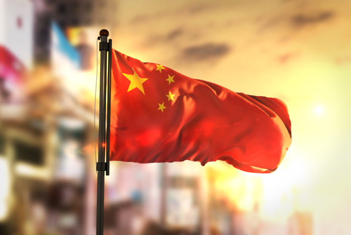 China Flag Against City Blurred Background At Sunrise Backlight