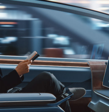 Futuristic Concept: Businessman in Glasses Reading Notebook and Watching News on Augmented Reality Screen while Sitting in a Autonomous Self-Driving Zero-Emissions Car.