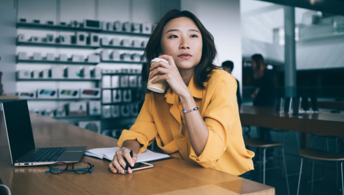 Asian woman drinking coffee and thinking at desk